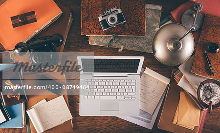 Messy vintage desktop with laptop, phone, lamp, camera and folders, top view