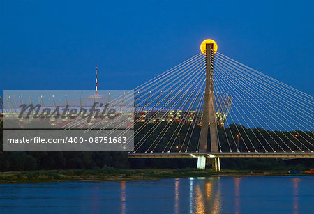 Warsaw, Poland - July 20, 2016: Panoramic view of the rising fullmoon over the National Stadium and Swietokrzyski Bridge in Polish Capital. In the blue waters of the Vistula reflected lights at night.