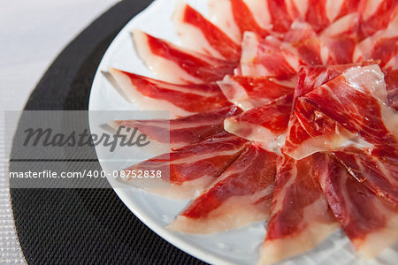 Circular decorative arrangement of iberian cured ham on plate. Selective focus point