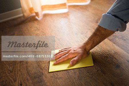 Male hand cleaning and rubbing an hardwood floor with a microfiber cloth.