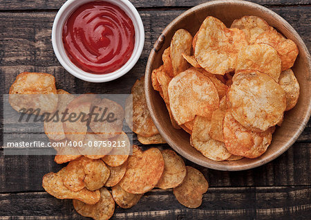Bowl with potato crisps chips and ketchup on wooden board. Junk food