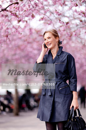 Young woman with cell phone near cherry blossom trees