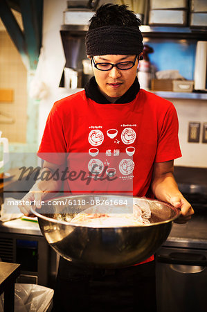 The ramen noodle shop. A chef preparing a huge metal bowl of broth with meat ingredients.
