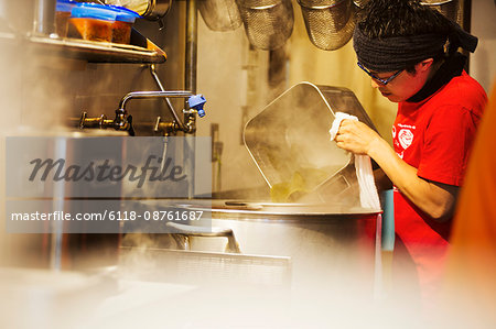 The ramen noodle shop. A chef working in a kitchen preparing food using a stove and large pans.