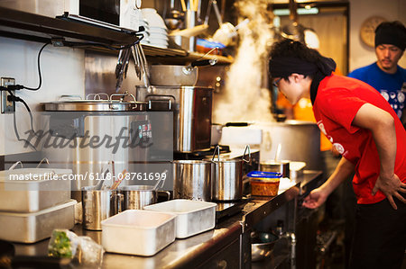 The ramen noodle shop.  Staff preparing food in a tiny kitchen