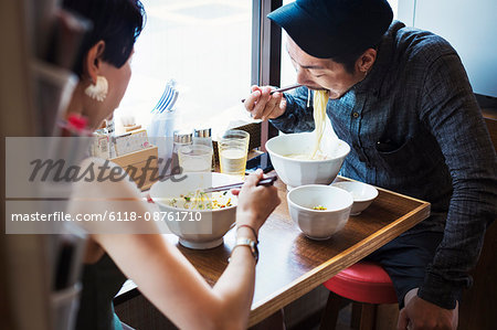 A ramen noodle cafe in a city.  A man and woman seated eating noodles from large white bowls.