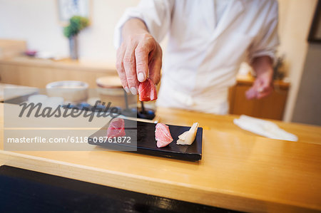 A chef working in a small commercial kitchen, an itamae or master chef presenting a fresh plate of sushi.