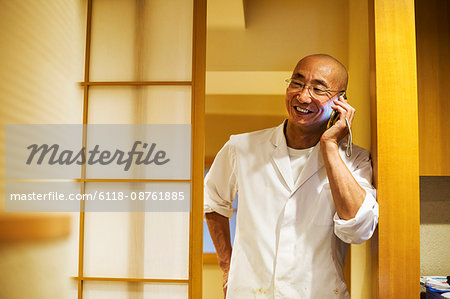 A chef  in a small commercial kitchen, an itamae or master chef on his smart phone.