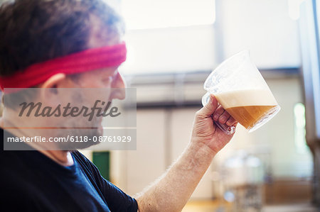 A brewer with a red bandana taking a jug of brewing beer and examining it.