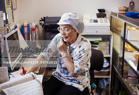 A mature woman at a desk in the office of a noodle production factory on the telephone.