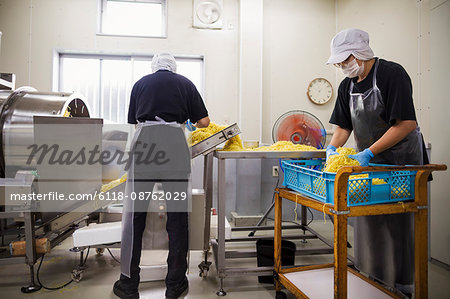 Workers in aprons and hats collecting freshly cut noodles from the conveyor belt to package and sell.