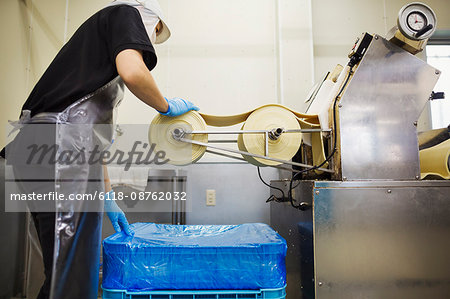 A Soba noodle factory.  Sheets of fresh noodle dough being passed through a large pressing machine.