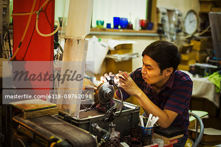 A craftsman at work sitting using a grinding machine to etch and mark a pattern on a glass object.