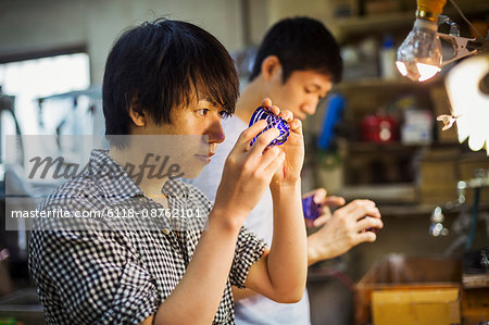 A craftsman at work in a glass maker's workshop working on a vivid blue cut glass object.