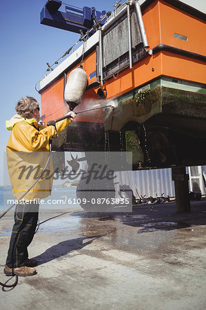 Man cleaning boat with pressure washer on a sunny day