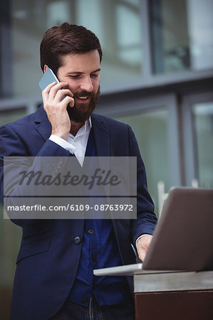 Businessman talking on mobile phone while using laptop