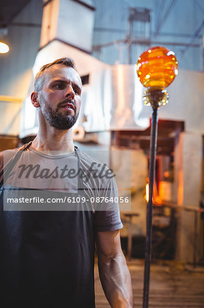 Glassblower shaping a molten glass at glassblowing factory