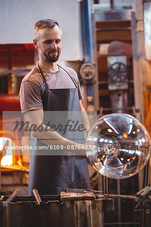 Glassblower shaping a molten glass at glassblowing factory