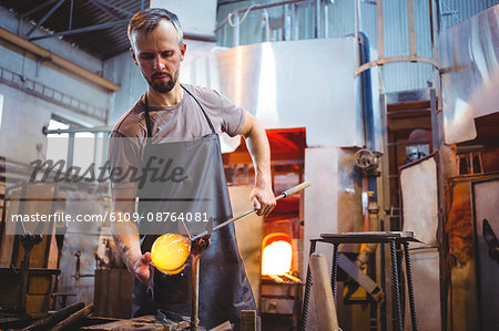 Glassblower forming and shaping a molten glass at glassblowing factory