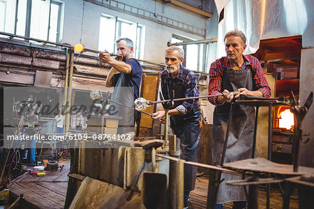 Team of glassblower shaping a glass on the blowpipe at glassblowing factory