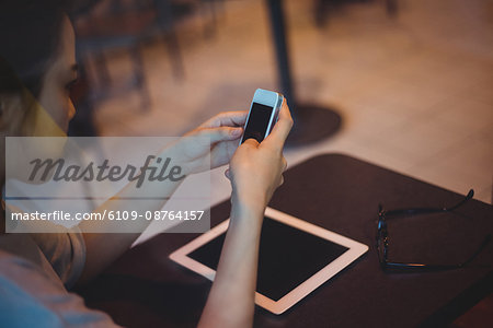 Woman text messaging on mobile phone in café