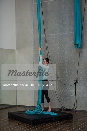Gymnast holding blue fabric rope on landing mat in fitness studio
