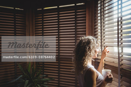 Thoughtful woman looking through window in living room at home