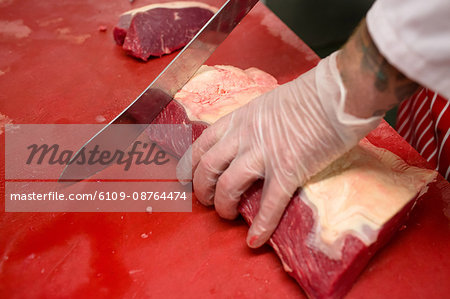 Hands of butcher slicing red meat at butchers shop