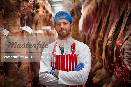 Portrait of butcher standing with arms crossed in meat storage room at butchers shop Portrait of butcher standing with arms crossed in meat storage room at butchers shop