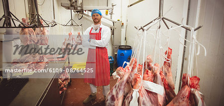Portrait of butcher standing with arms crossed in meat storage room at butchers shop