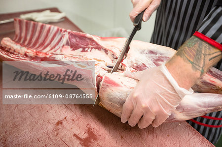 Mid section of butcher cutting the ribs of pork carcass in butchers shop