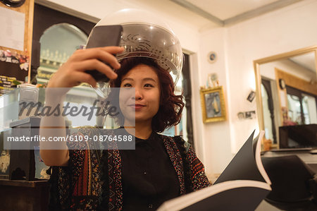 Stylish woman taking a selfie while sitting under a hairdryer at hair salon