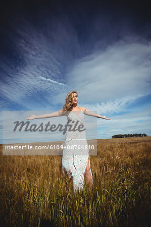 Woman standing with arms outstretched in wheat field on a sunny day