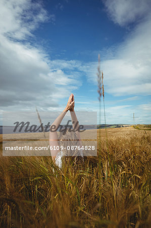 Woman with hands raised over head in prayer position in field on a sunny day