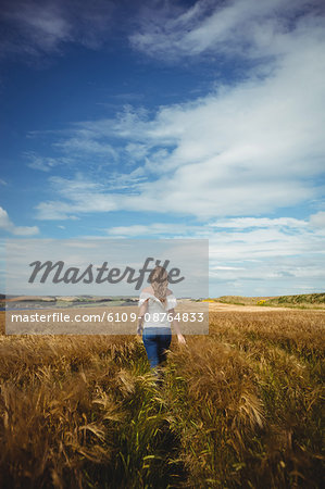 Rear view of woman walking through wheat field on a sunny day