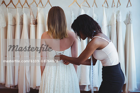 Woman trying on wedding dress with the assistance of fashion designer in the studio