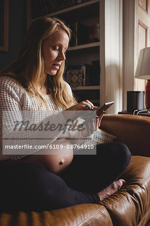Pregnant woman using mobile phone in living room at home