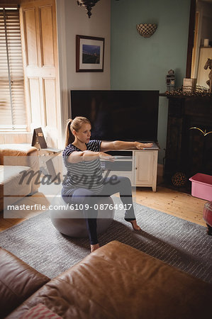 Pregnant woman performing stretching exercise on fitness ball in living room at home