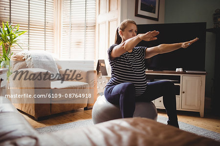 Pregnant woman performing stretching exercise on fitness ball in living room at home