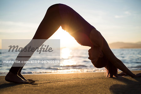 Woman performing yoga on beach during sunset