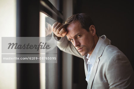 Thoughtful businessman leaning on window at office