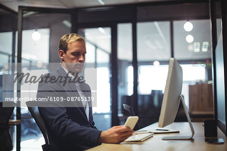 Businessman using mobile phone while sitting at desk in office