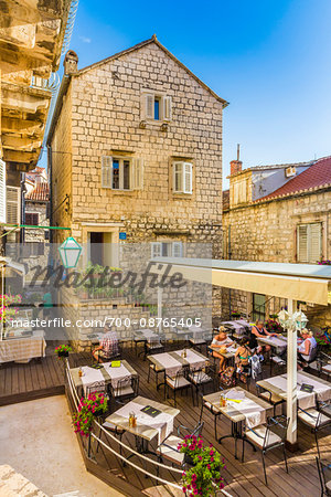 People sitting in a restaurant patio behind a stone building in the Old Twon of Hvar on Hvar Island, Croatia