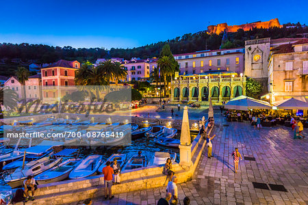 Boats docked at marina with the Venetian Loggia and the Hvar Fortress overlooking the harbour at dusk in the Old Town of Hvar on Hvar Island, Croatia