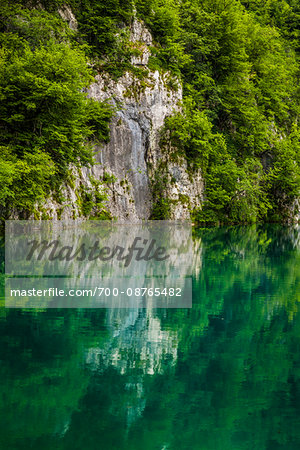 Rock cliff and trees reflected in emerald green lake water at the Plitvice Lakes National Park in Croatia