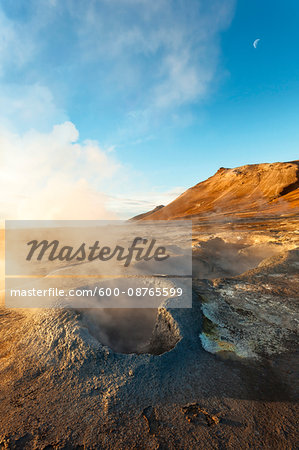 Sunlit mist rising from the Hverir Hotsprings on Namafjall with the moon in the blue sky, Northeast Iceland Sunlit mist rising from the Hverir Hotsprings on Namafjall with the moon in the blue sky, Northeast Iceland
