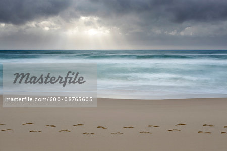 Cloudy sky with crepuscular sunrays over the Tyrrhenian Sea and footprints in the sand on the beach at San Felice Circeo in the Province of Latina in Latina in Lazio, Italy