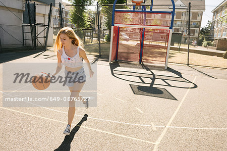 Young woman running with ball on basketball court