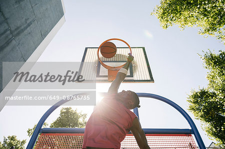 Young male basketball player throwing ball in sunlit basketball hoop