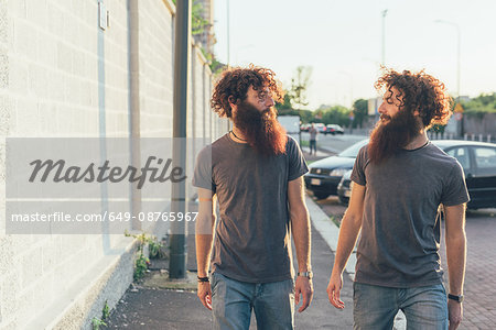 Identical male adult twins strolling and chatting on sidewalk